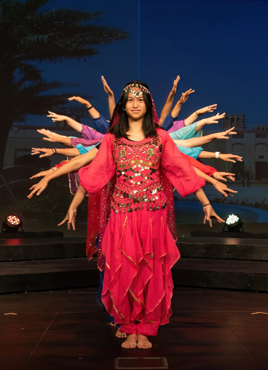 A young performer centre stage in costume, dancers behind her